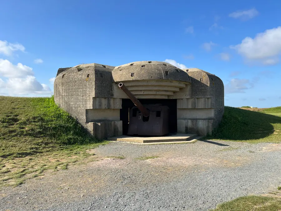 A weathered concrete casemate at Longues-sur-Mer with the barrel of a 150mm naval gun protruding.