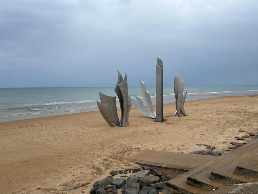 The stainless steel wings of the Les Braves sculpture rising from the sand at Omaha Beach.