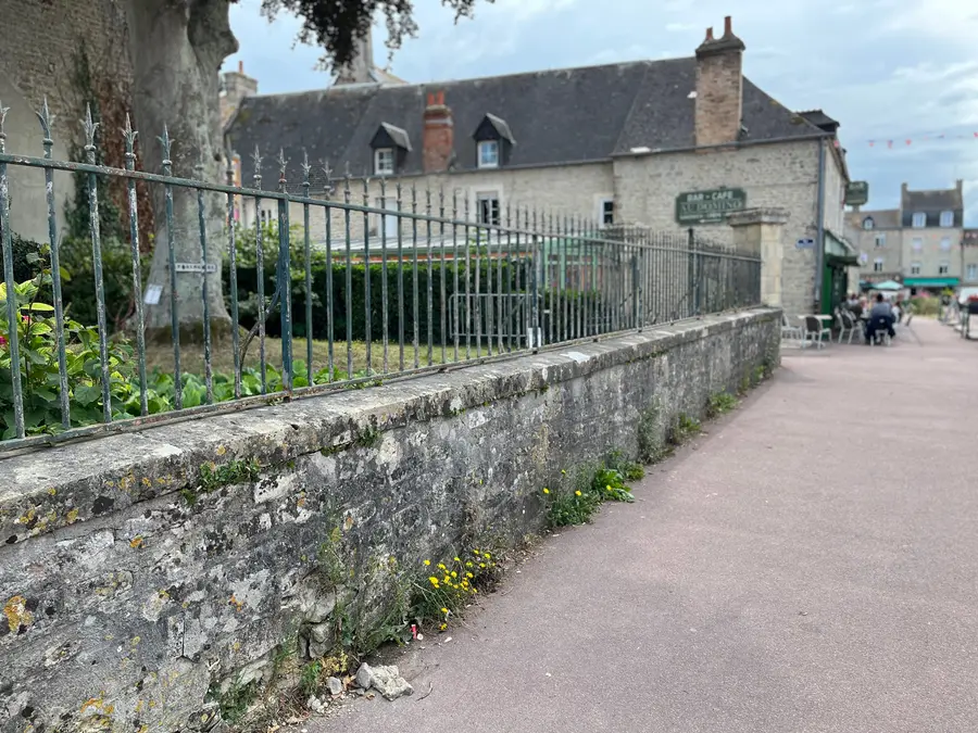 A street of pale stone buildings in Sainte-Mère-Église on a bright day, flags hanging from the façades.