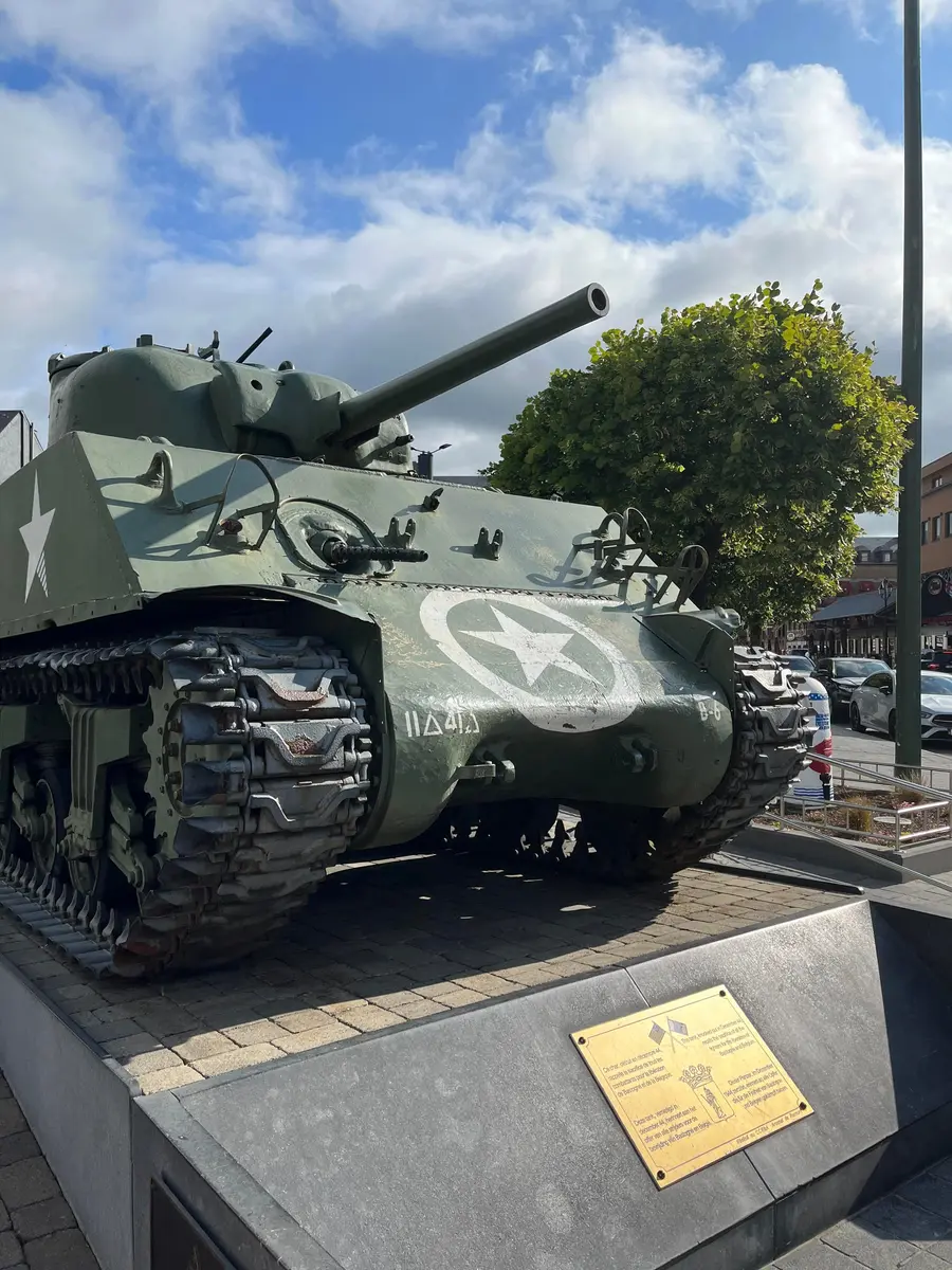 A Sherman tank displayed on a plinth in Bastogne’s main square in evening light.