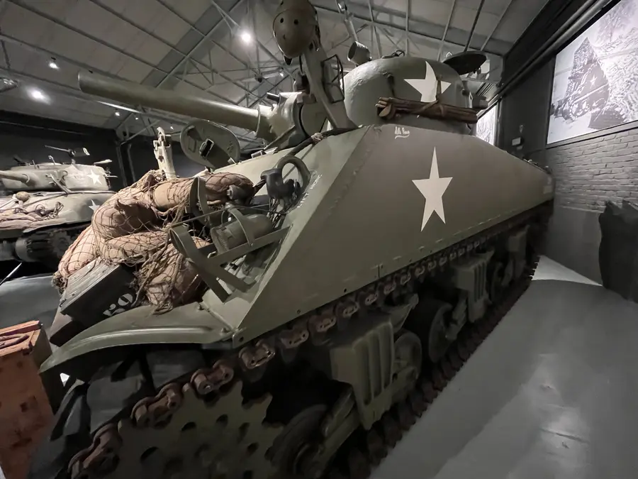 A fully restored Sherman tank in olive drab inside a museum hall.